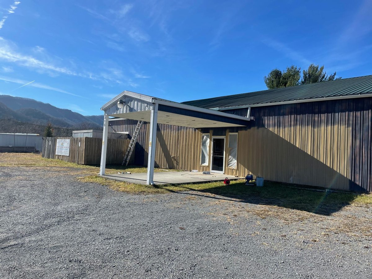 Metal building before — chalked, sun-faded steel siding and a bare canopy frame